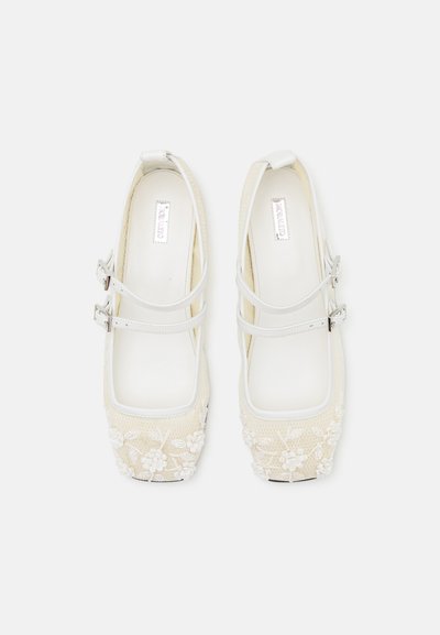 Chaussures plates blanches à broderie florale avec double brides, design à bout carré et matière supérieure texturée. Accentuée d'une finition lisse blanche.