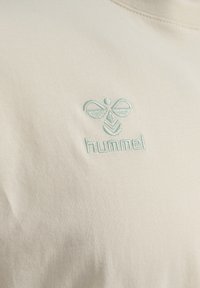 Creme T-shirt lavet af ribbet bomuld, med et let blåt broderet bi-logo og brandnavnet "hummel" under det.