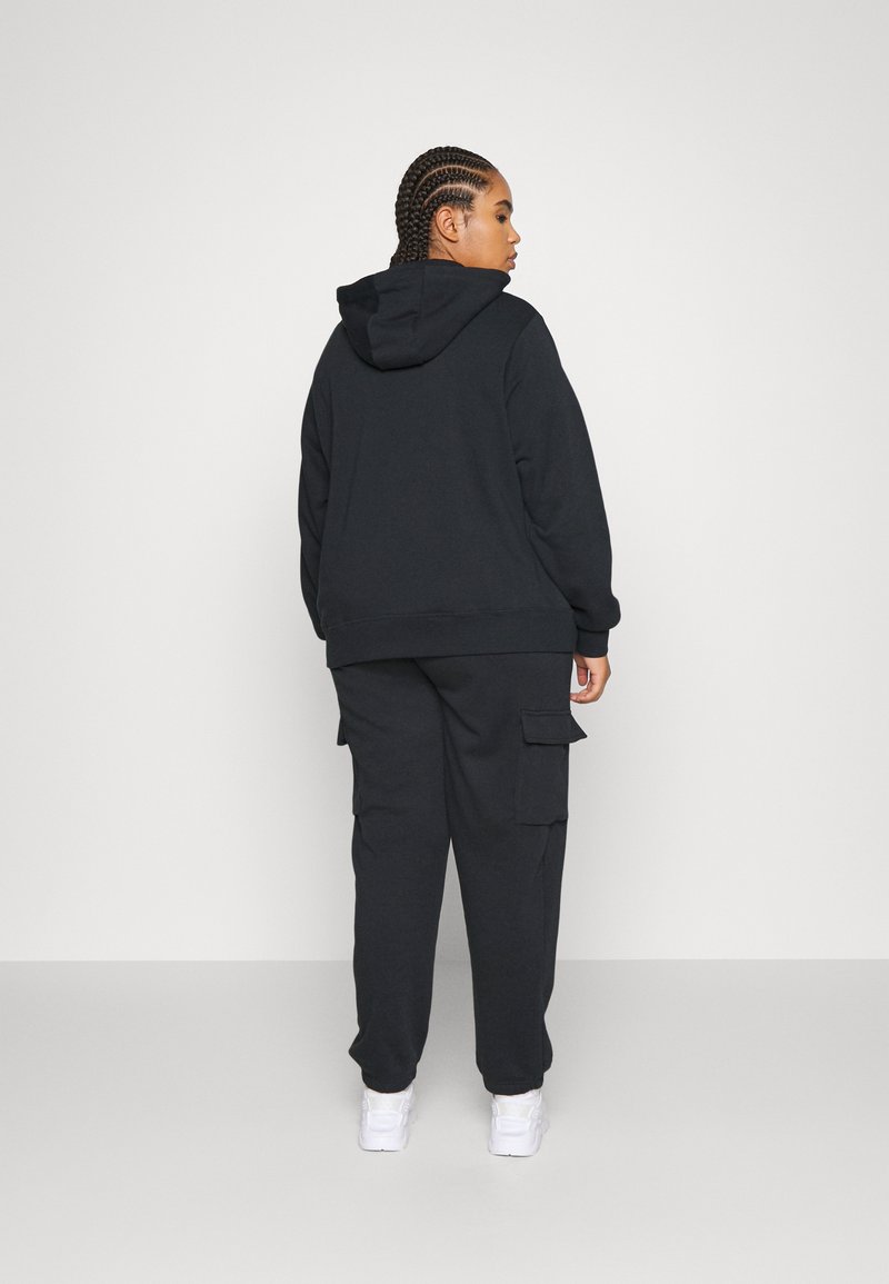 Sudadera negra con capucha ajustable, combinada con pantalones cargo a juego que tienen bolsillos laterales, ambos hechos de tela suave. Se llevan zapatillas blancas.