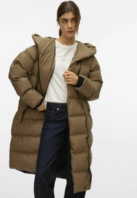 Langer brauner Puffer-Mantel mit Kapuze, gesteppter Musterung, vorderem Reißverschluss und Druckknöpfen. Kombiniert mit einem weißen T-Shirt und dunklen Jeans.