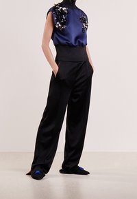 Marinblus i satin med blomsterdetaljer i paljetter, högmidjade svarta byxor, stilren design, avslappnad passform och svarta skor med blå accenter.