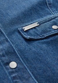 Camicia di jeans di blu medio, con un'etichetta metallica ALLSAINTS, bottoni argento e un colletto classico con dettagli di cucitura.