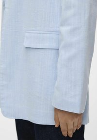 Veste bleu clair avec un tissu lisse et texturé. Comprend une poche avant et une coupe décontractée avec des manches droites, présentée de côté.