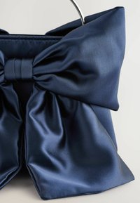 Marine satin håndtaske med en stor sløjfedetalje og sølv hardware. Overfladen er glat og blank, hvilket fremhæver elegante folder og tekstur.
