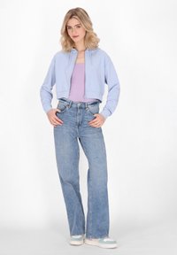Felpa corta blu chiaro con coulisse, indossata sopra una maglietta lavanda. Jeans blu a vita alta e a vestibilità ampia, abbinati a sneakers multicolori.