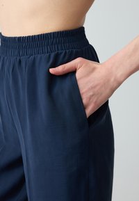 Marineblaue, leichte Hosen mit elastischem Bund und Seitentaschen. Glatte Textur mit lockerer Passform.