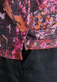 Wielokolorowa koszulka sportowa z różowym, pomarańczowym i szarym abstrakcyjnym wzorem kwiatowym. Materiał jest miękki, z widocznymi detalami szycia.