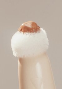 Behälter mit einer glatten, beigen Basis, bedeckt von einer runden, schokoladenfarbenen Kuppel und umgeben von einer fluffigen weißen Textur.