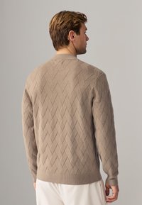 Beige gestrickter Pullover mit einem strukturierten Rautenmuster, geripptem Kragen, Bündchen und Saum. Die Rückansicht zeigt deutliche Nähdetails.