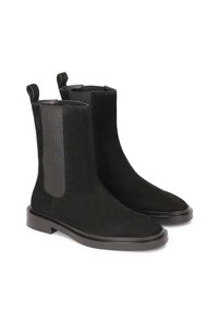 Un par de botas Chelsea negras de ante con paneles laterales elásticos y tiradores, que presentan tacones bajos y puntas redondeadas sobre un fondo blanco.