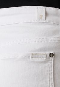 Valged denim püksid hõbedase nööbi, õmmeldud sildiga ja tekstureeritud kangaga, sirge lõikega disainiga.