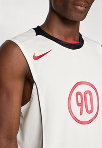 Ermeløs hvit sportstrøye med svart kragekant, rød Nike-sva på skulderen, og rød nummer 90 inne i en sirkel på brystet.