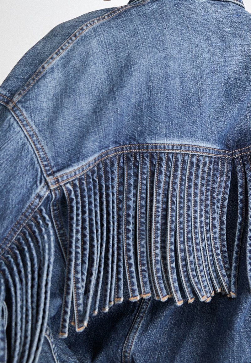 Dos d'une veste en jean bleue avec des détails plissés verticaux et des surpiqûres contrastantes orange le long des coutures.