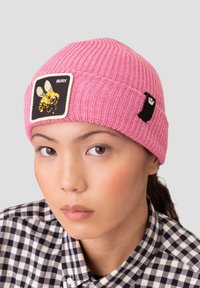 Pink ribbed beanie with an embroidered black patch depicting a bee and the word "BUSY." Additional black logo accent on the side.