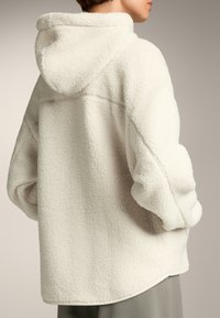 Felpa bianca in pile con superficie texture, grande cappuccio e spalle scese. Presenta una vestibilità rilassata e orlo curvo.