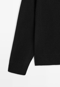 Czarny sweter z dzianiny z mankietem prążkowanym, prezentujący miękką teksturę i prosty, minimalistyczny design. Brak widocznych wzorów lub ozdób.