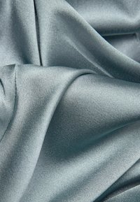 Tela de satén azul claro con una textura suave y brillante. El material se drapea elegantemente, mostrando pliegues sutiles y un suave brillo.
