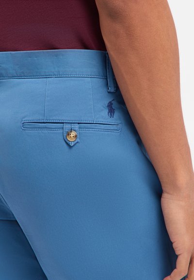 Jasnoniebieskie spodnie z mieszanki bawełny, z płaską tylną kieszenią ozdobioną złotym guzikiem i haftowanym granatowym logo. Gładka faktura i dopasowany krój.