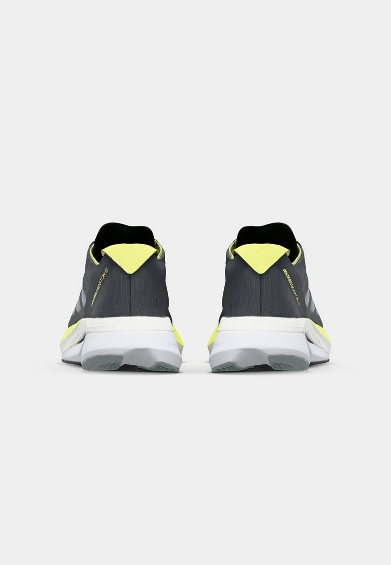 Szare buty sportowe z żółtymi akcentami oraz teksturowaną siateczką, z wyściełaną podeszwą i uchwytem na pięcie ułatwiającym zakładanie.