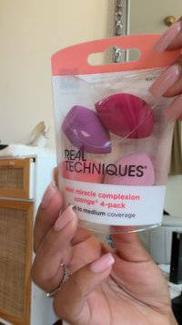 Mini spugnette per il viso in colori rosa, viola e corallo, confezionate in modo sicuro in un contenitore di plastica trasparente con etichetta "Real Techniques."