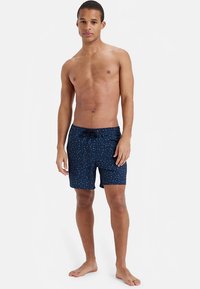 Mornarsko modre kopalne hlače z vzorcem pik, elastičnim pasom in vrvico za zavezovanje. Tkanina je videti lahka in hitro sušeča.