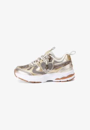 Masywne sneakersy ze złotym metalicznym materiałem w pepitkę, masywną białą podeszwą, beżowymi sznurówkami i srebrną zawieszką w kształcie serca przymocowaną do sznurówek.