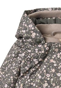 Tummavihreä, kukkakuviollinen takki, jossa on vaaleanpunaisia ja valkoisia kukkia. Takissa on korkea kaulus, beige resorivuori ja nepparikiinnitys.