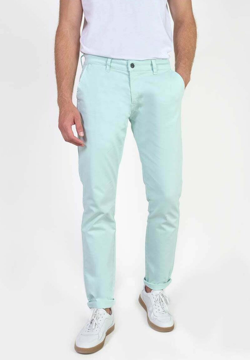 Chinos vert menthe clair en coton avec une coupe slim, dotés d'une fermeture à bouton et de poignets retroussés, associés à des baskets blanches.