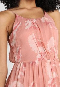 Rosa blommig klänning med texturerat tyg, justerbara spaghettistövlar och en avslappnad passform. Har en rynkad midja och mjuk, flödande kjol.