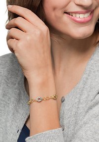 Gold-tone bracelet with linked oval and round chain elements. Smooth metal finish with a shiny texture, worn on a wrist.