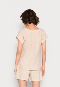 Blusa beige a maniche corte con scollo rotondo, tessuto testurizzato e dettaglio arricciato sul retro; abbinata a pantaloni corti beige coordinati.