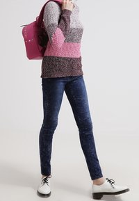 Strickpullover mit horizontalen Streifen in Grau, Pink und Burgunderrot. Kombiniert mit dunkelblauen Jeans und weißen Schnürschuhen. Rosa Rucksack getragen.