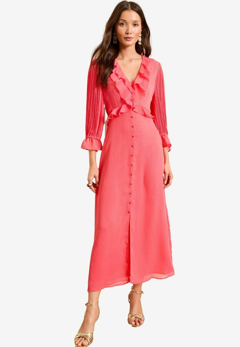 Abito plissettato corallo con scollatura arricciata, maniche lunghe, chiusura con bottoni e gonna fluida: tessuto leggero, texture morbida e design al ginocchio.