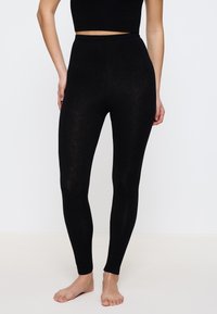 Zwarte leggings met een hoge tailleband, gemaakt van een zachte, rekbare stof, met een gladde textuur en zonder zichtbare naden of patronen.