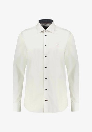 Chemise habillée blanche à manches longues avec boutons noirs et petit logo brodé sur le côté gauche de la poitrine.