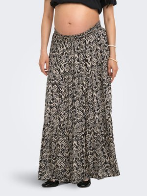 Femme portant une jupe longue noire et beige à motifs, des ballerines noires et un haut noir relevé révélant sa taille et son ventre.
