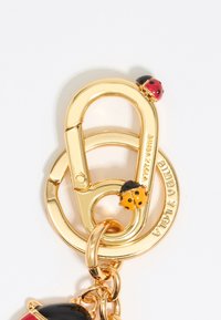 Gold metal keychain featuring a clasp with a circular ring. Two ladybug accents in red and black and yellow, with a logo on the ring.