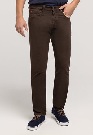 Brązowe bawełniane spodnie o prostym kroju, z pięcioma kieszeniami i widoczną metką marki. W zestawie z granatowymi tenisówkami.