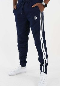 Navy joggingbroek met witte zijstrips en een logo op de bovenbenen. Gemaakt van een zacht materiaal, met een elastische tailleband en enkelboorden.