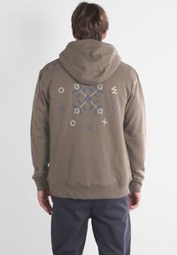 Hoodie vert olive avec une capuche à cordon et un design à motifs au dos en bleu et crème. Tissu doux avec des poignets et un ourlet côtelés.