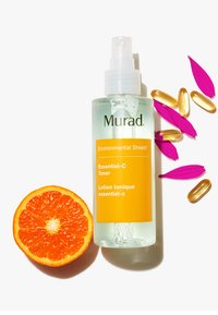 Le tonique Essential-C de Murad Environmental Shield dans une bouteille claire avec un vaporisateur blanc, arborant une étiquette orange vif. Accompagné d'une moitié d'orange, de capsules et de pétales roses.