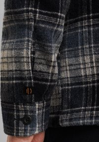 Ruudullinen paita tummansinisissä, harmaissa ja kermaisen sävyissä; villasekoitekangas; varustettu nappikiinnityksellä ja merkkilapulla hihassa.