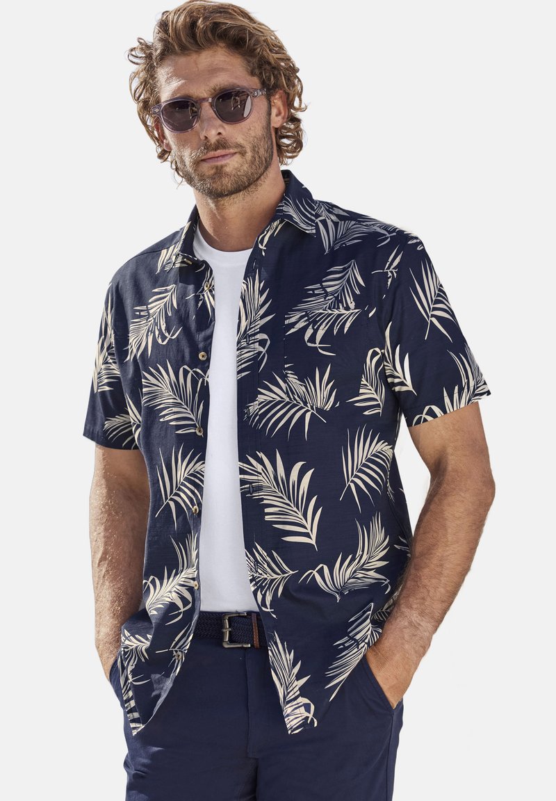 Camisa de manga corta azul marino con patrón de hojas de palma color crema, cuello abotonado y corte recto, llevada sobre una camiseta blanca de cuello redondo.