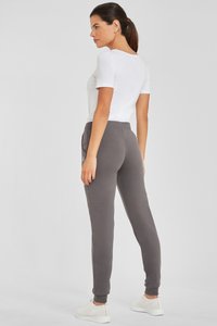 Graue Sweatpants mit elastischem Bund und Bündchen, kombiniert mit einem weißen, eng anliegenden T-Shirt. Dazu gehören weiße, strukturierte Sneakers.