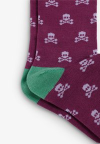 Calcetines morados con un patrón repetido de calaveras y huesos cruzados blancos, con acentos verdes en el talón y la puntera, hechos de material de punto suave.