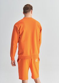 Pomarańczowy sweter z długimi rękawami i ściągaczami, w parze z pasującymi szortami. Oba mają gładką fakturę i sportowy design.