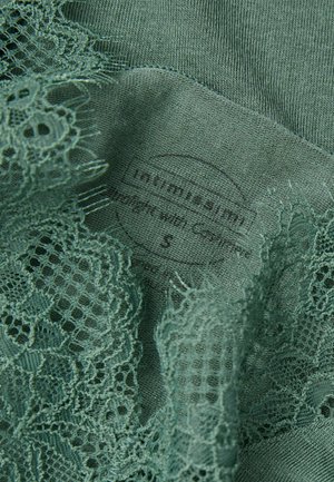 Mörkgrön tyg med intrikata spetsdetaljer och en mjuk textur, med en synlig etikett som anger "Intimissimi" och storlek 'S.'