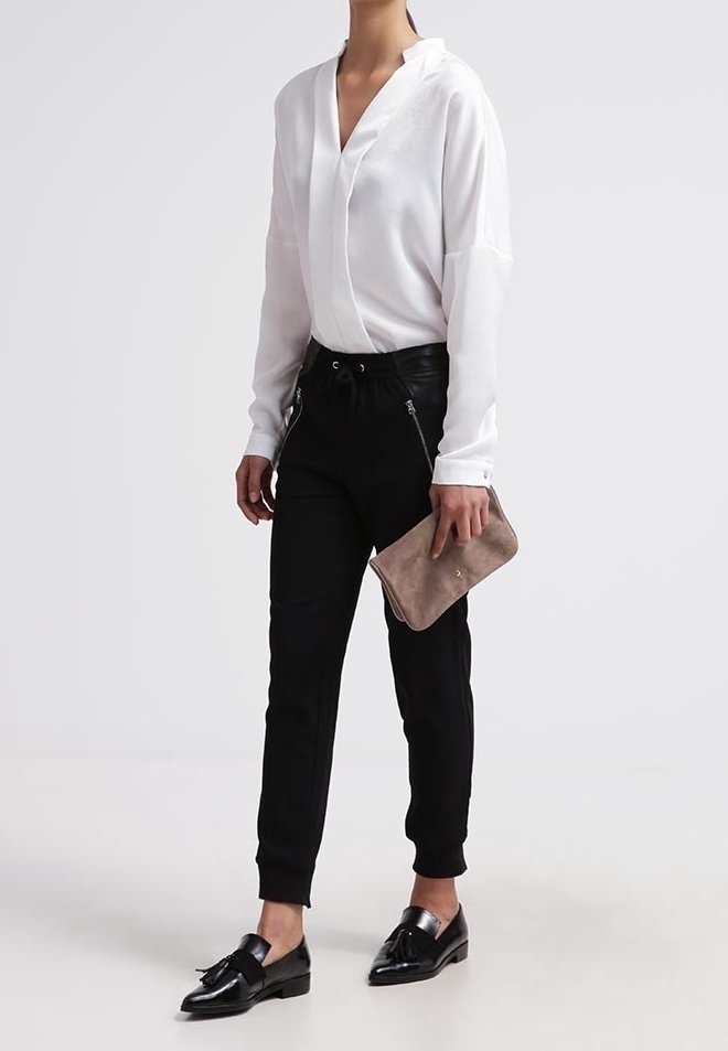 Hvid langærmet bluse med V-hals, sorte tapered bukser med lynlåse, sorte sko, holder en beige clutch. Glat stof, rene linjer.