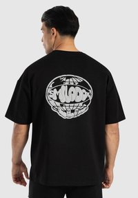 Camiseta de algodón negra con mangas cortas, que presenta un gran gráfico blanco de un globo y manos en la parte posterior. Diseño simple, ajuste relajado.