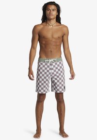 Checkered swim trunks in light brown and white, with a green waistband, drawstring closure, and a square pattern.